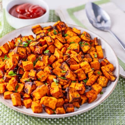 Easy air fryer sweet potato cubes plated with parsley garnish and a small bowl of ketchup on the side.