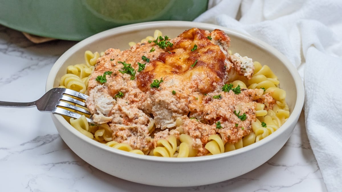 Wide image of the plated baked ricotta chicken casserole recipe served in a tan pasta bowl.