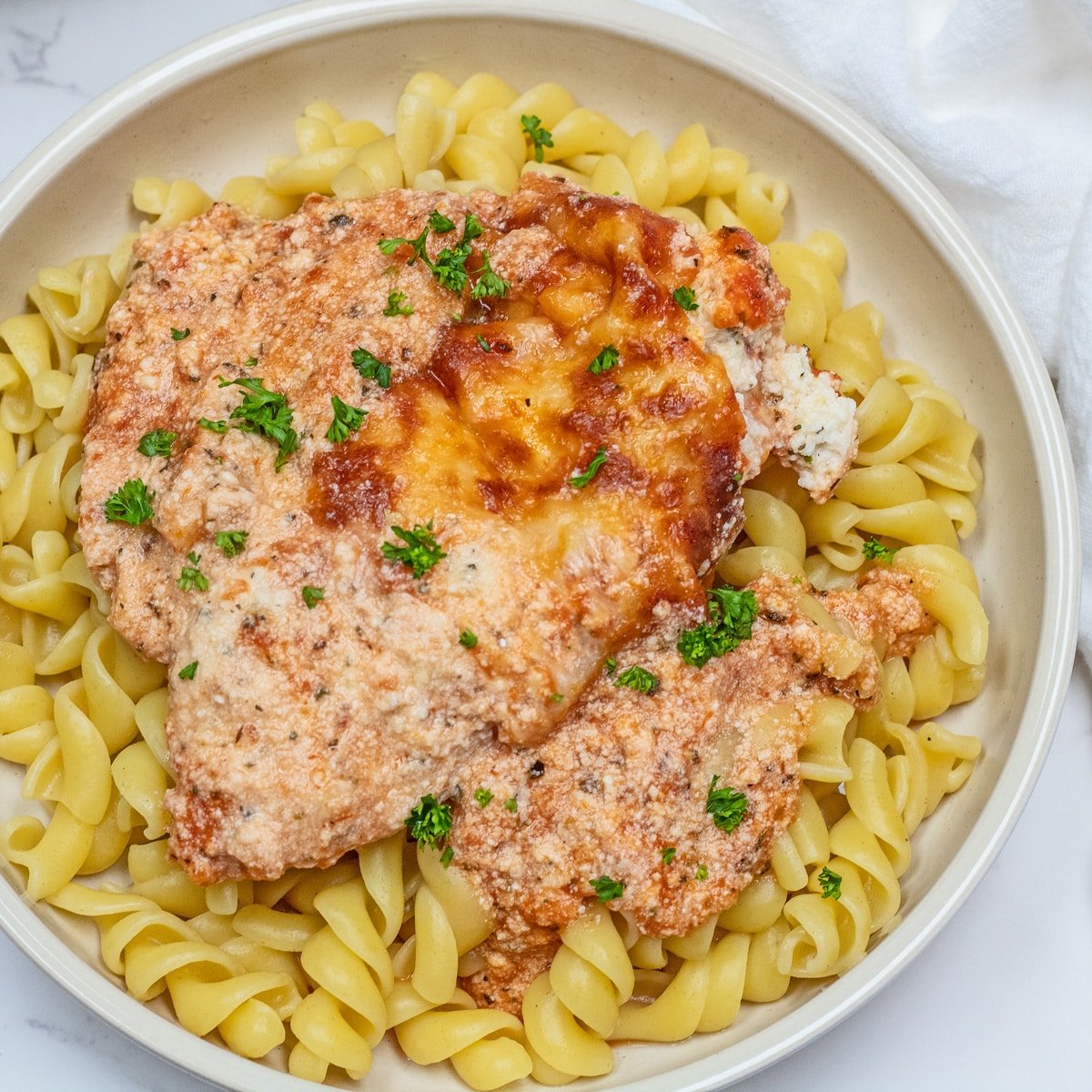 Tasty baked ricotta chicken recipe dished up on a light tan plate with pasta.