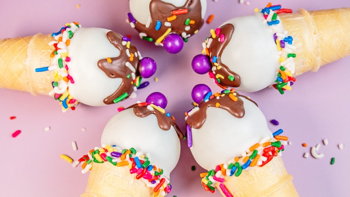 Wide overhead image of the ice cream cake pop tops in a circle on lavender background with loose sprinkles.