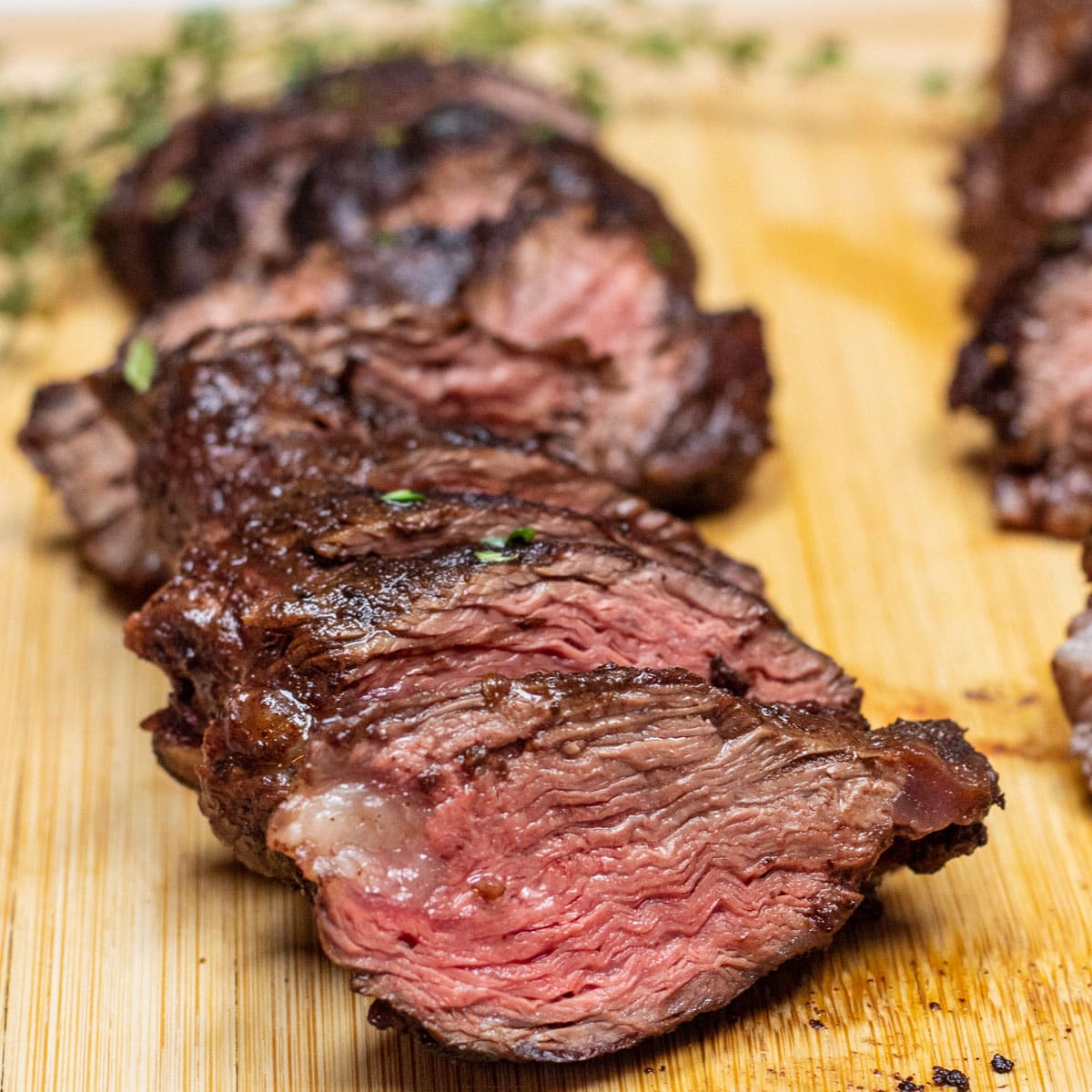 Square image of hanger steak on a cutting board, sliced.