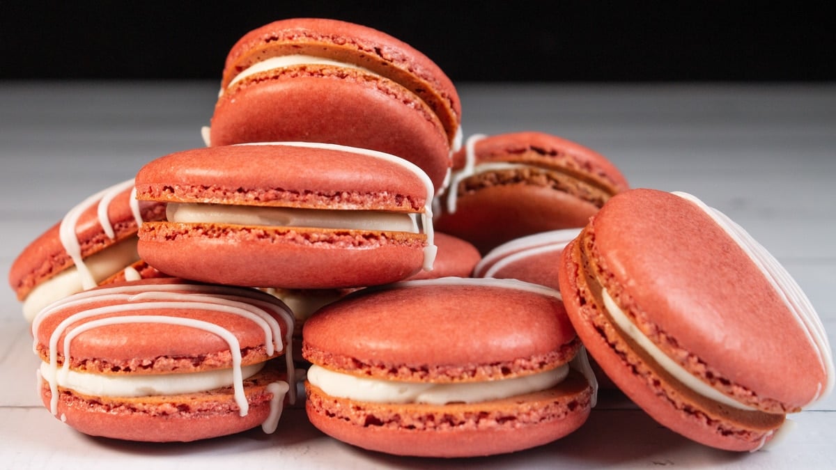 Wide image of the red velvet macarons randomly stacked on a light wooden grain surface.