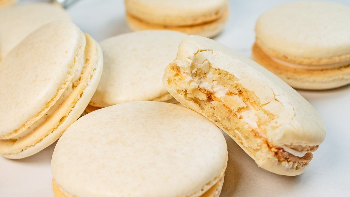 Best vanilla macaron recipe featuring a bitten macaron leaned against another assembled macaron cookie.