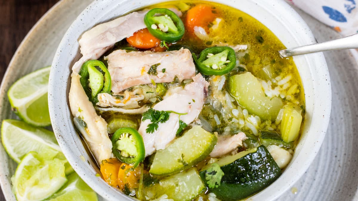 Wide image of a white bowl of caldo de pollo Mexicano.