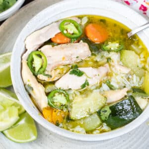 Square image of a white bowl of caldo de pollo Mexicano.