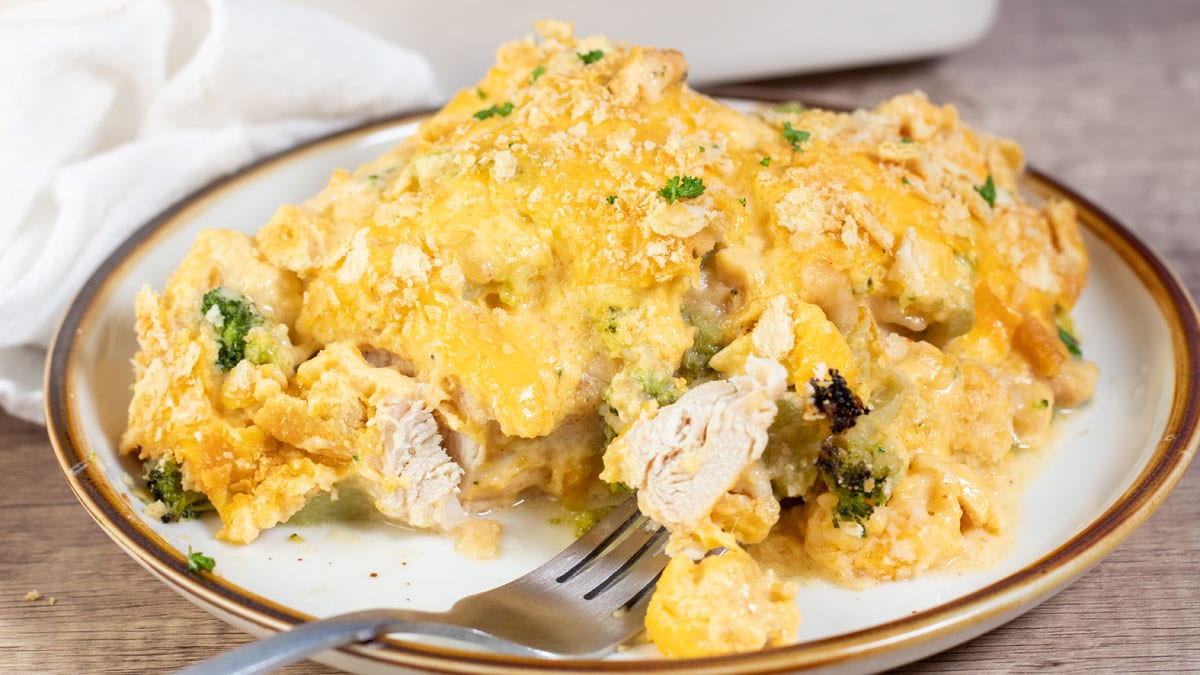 Wide closeup image of the plated Cracker Barrel broccoli cheddar chicken casserole with a forked bite at the front.