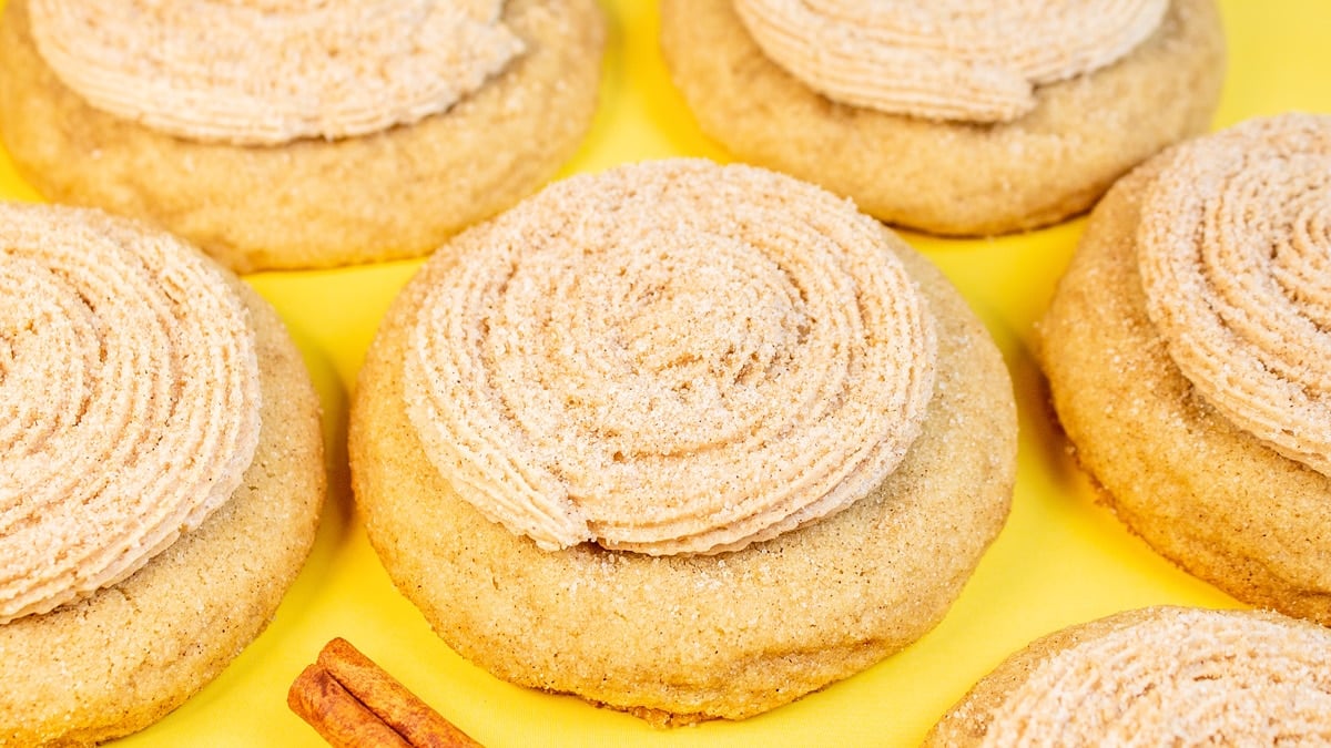 Best baked CRUMBL churro cookies arranged on a light yellow background with cinnamon sticks.