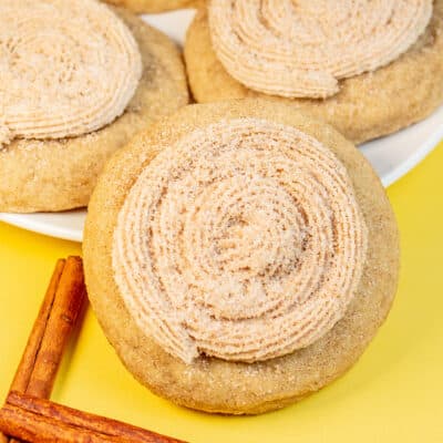 Best homemade CRUMBL churro cookies baked and decorated and served on a plate with some cinnamon sticks next to them.