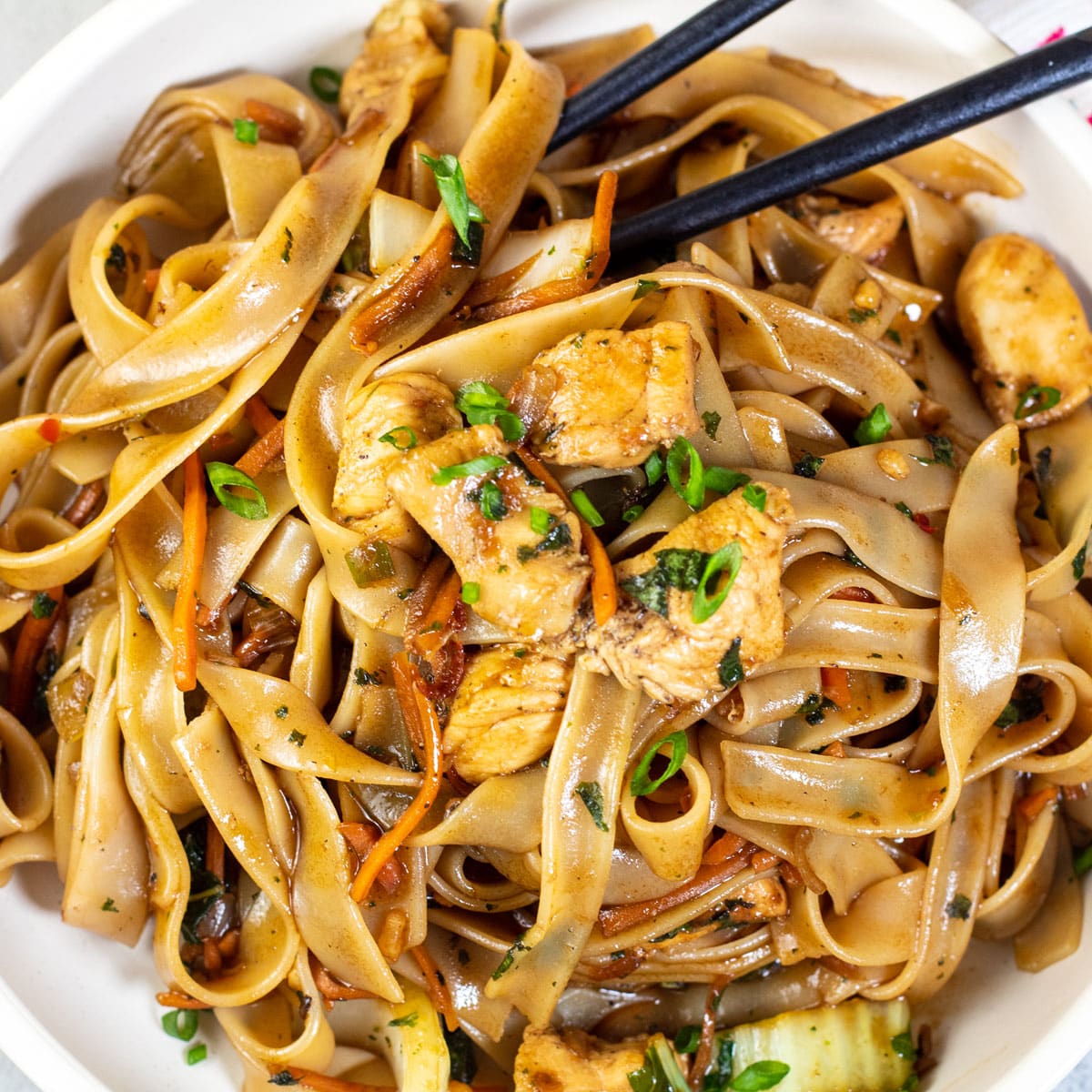 Square image of drunken noodles in a bowl with chop sticks.