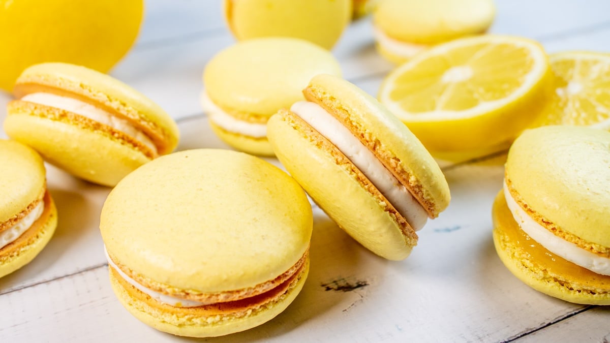 Tangy lemon macarons arranged randomly on light background with lemon slices.