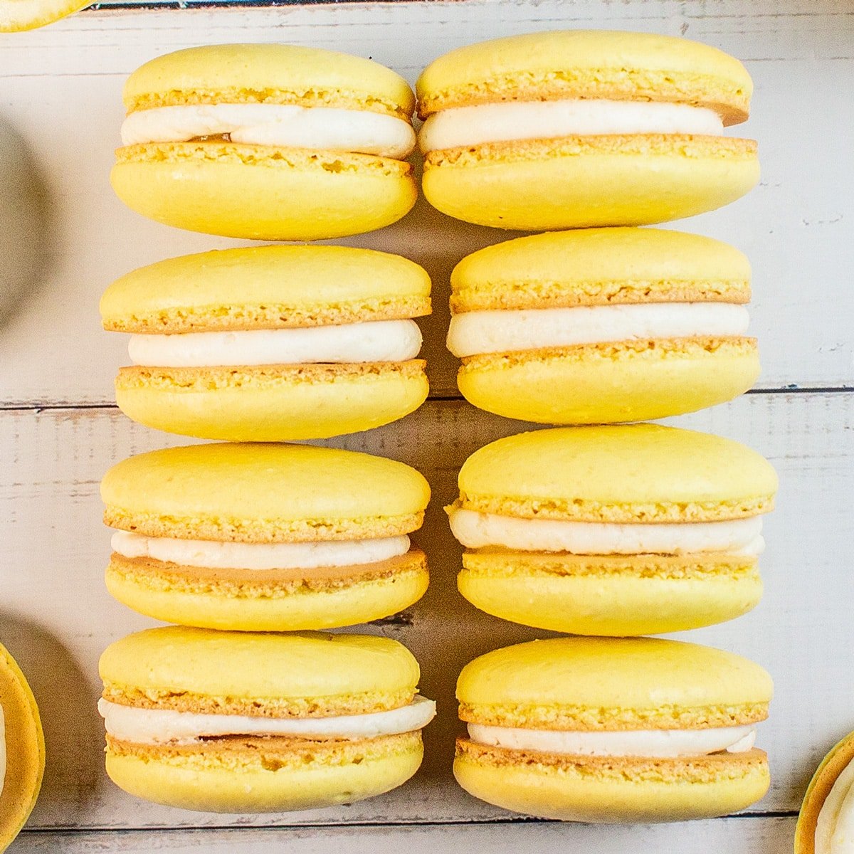 Tangy lemon macarons arranged in stacks on light wooden grain background.