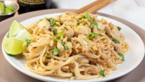 Wide image of pad thai on a white plate with chop sticks.