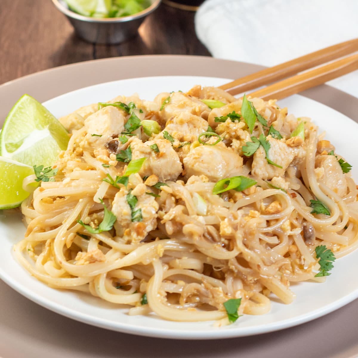 Square image of pad thai on a white plate with chop sticks.