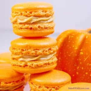 Square image showing two pumpkin macarons stacked on more macarons.