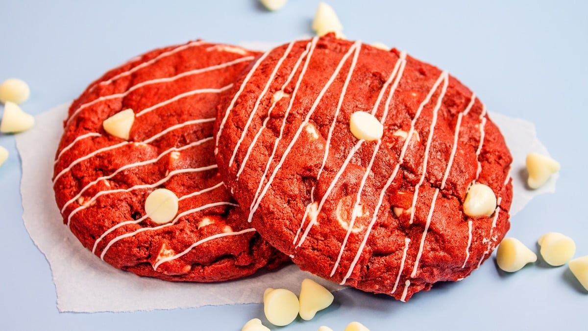 Delicious CRUMBL bakery style red velvet white chocolate chip cookies with some white chocolate drizzle and scattered chocolate chips.