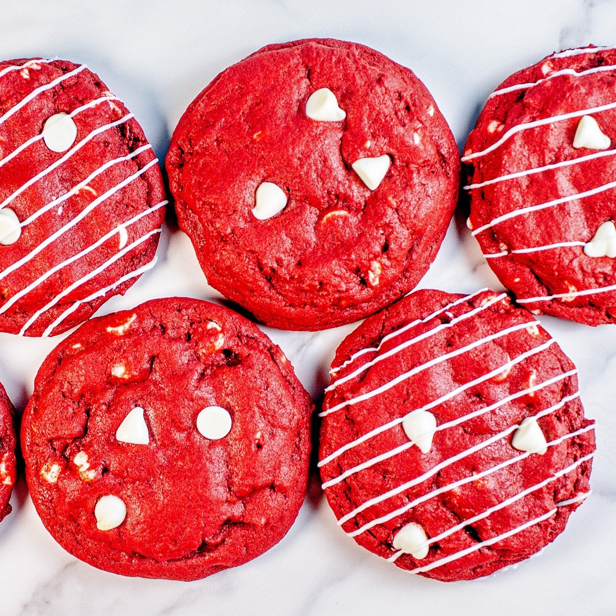 CRUMBL red velvet white chocolate chip cookies in rows, with a few drizzled with melted white chocolate strips.