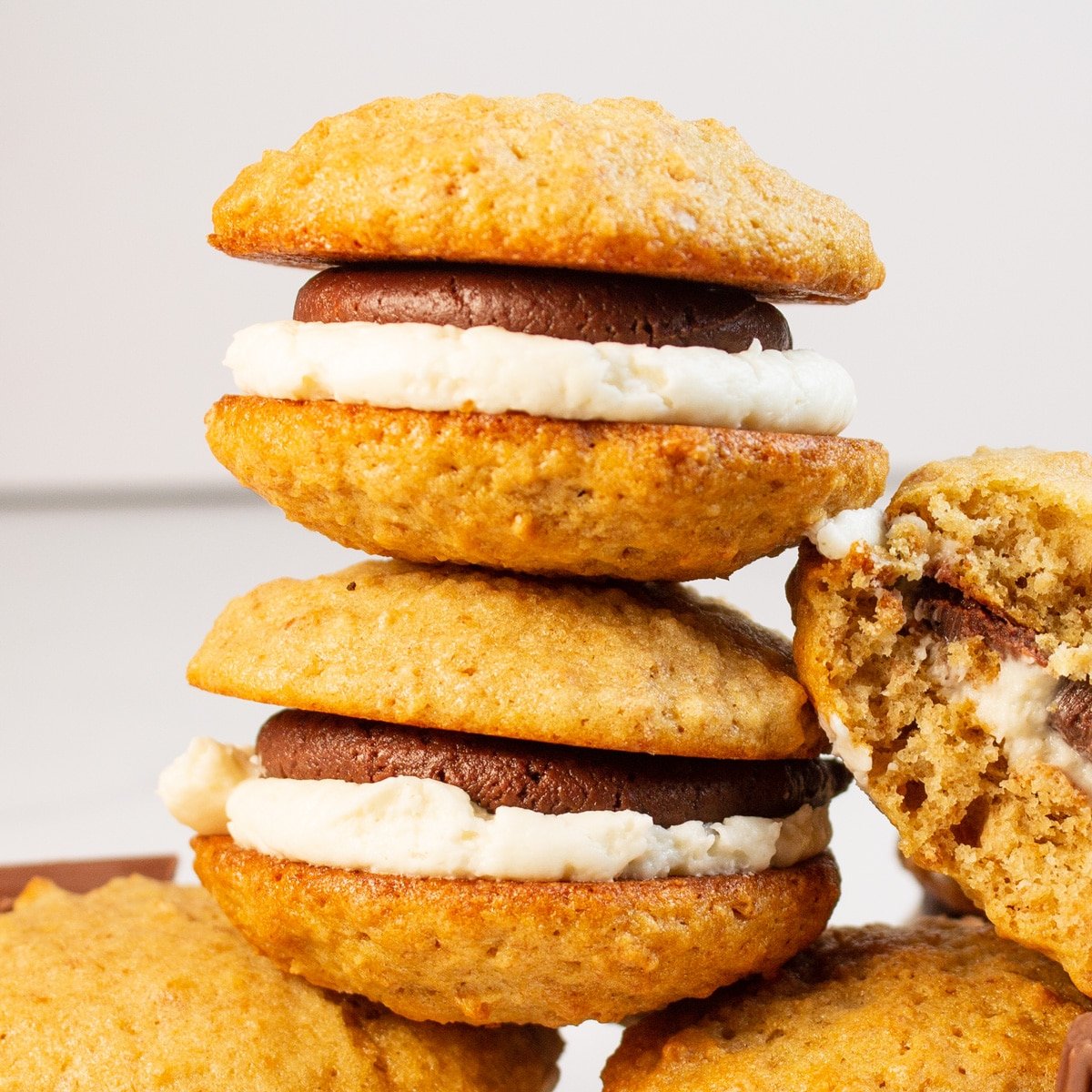 Tasty s'mores whoopie pies stacked on light background with a bitten cookie off to the right side.