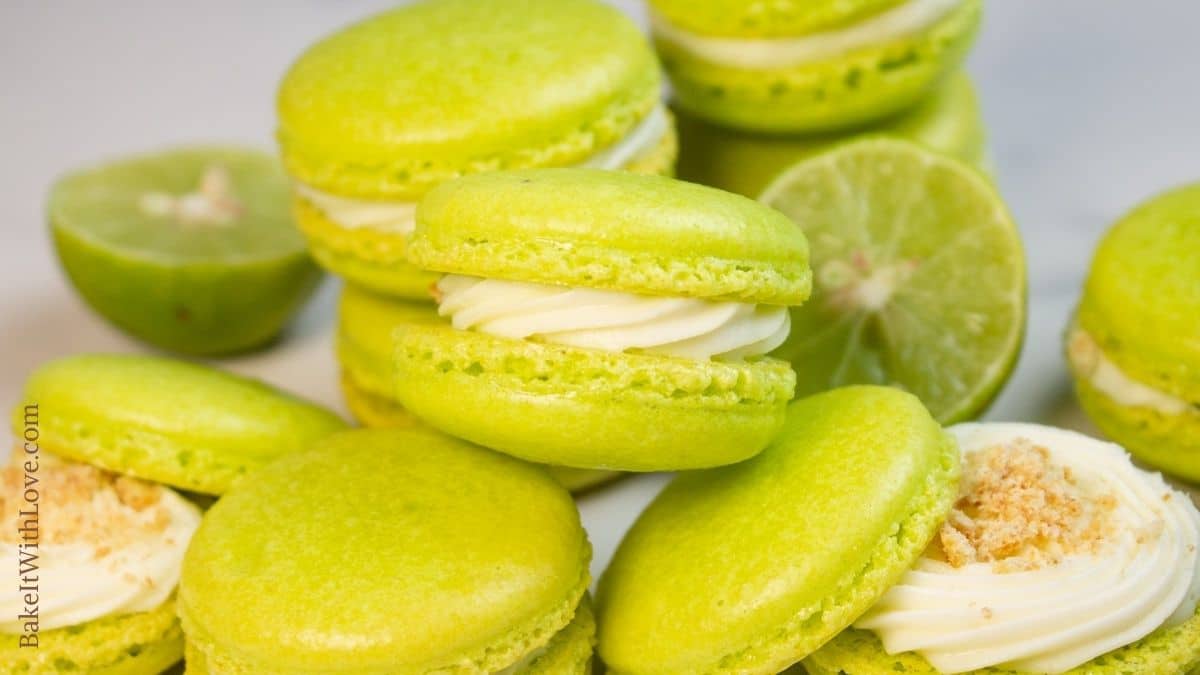 Tasty key lime macarons randomly stacked with halved limes in background.