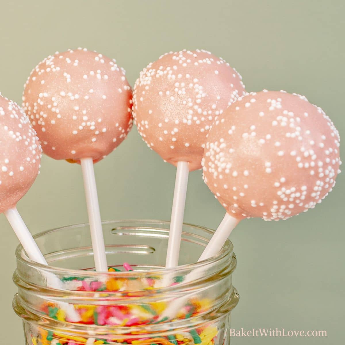 Four copycat Starbucks Birthday Cake Pops standing up in a glass jar filled with sprinkles.