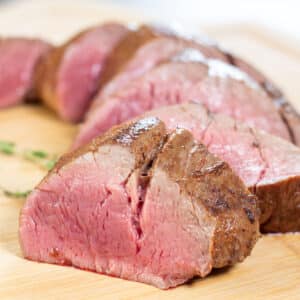 Tender, sliced venison tenderloin roast served on a light wooden cutting board.