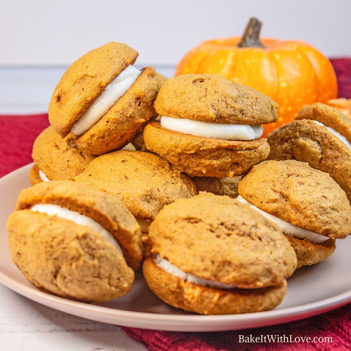 Best homemade pumpkin whoopie pies stacked on a white plate with pumpkin in the background.