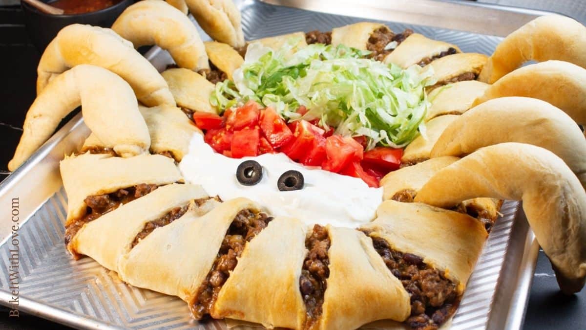 Spider taco ring on a baking sheet with taco toppings and olives for eyes. 