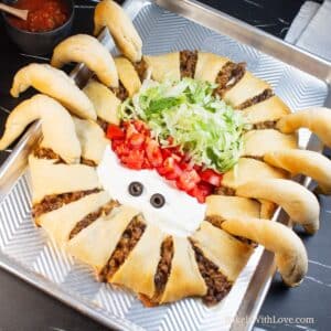 Spider taco ring on baking sheet with taco toppings in the body and sliced olives for eyes.