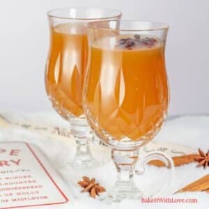 Best homemade apple cider recipe featuring two portions in crystal Irish coffee mugs and festive white holiday decor around them.