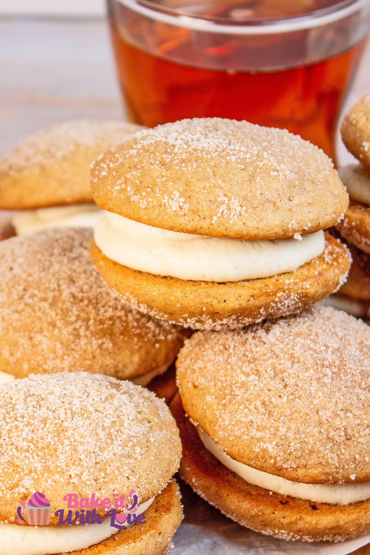 Tall image of apple cider whoopie pies with apple cider in the background. 