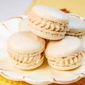 Square image showing three apple pie macarons stacked in a pyramid shape on a plate.