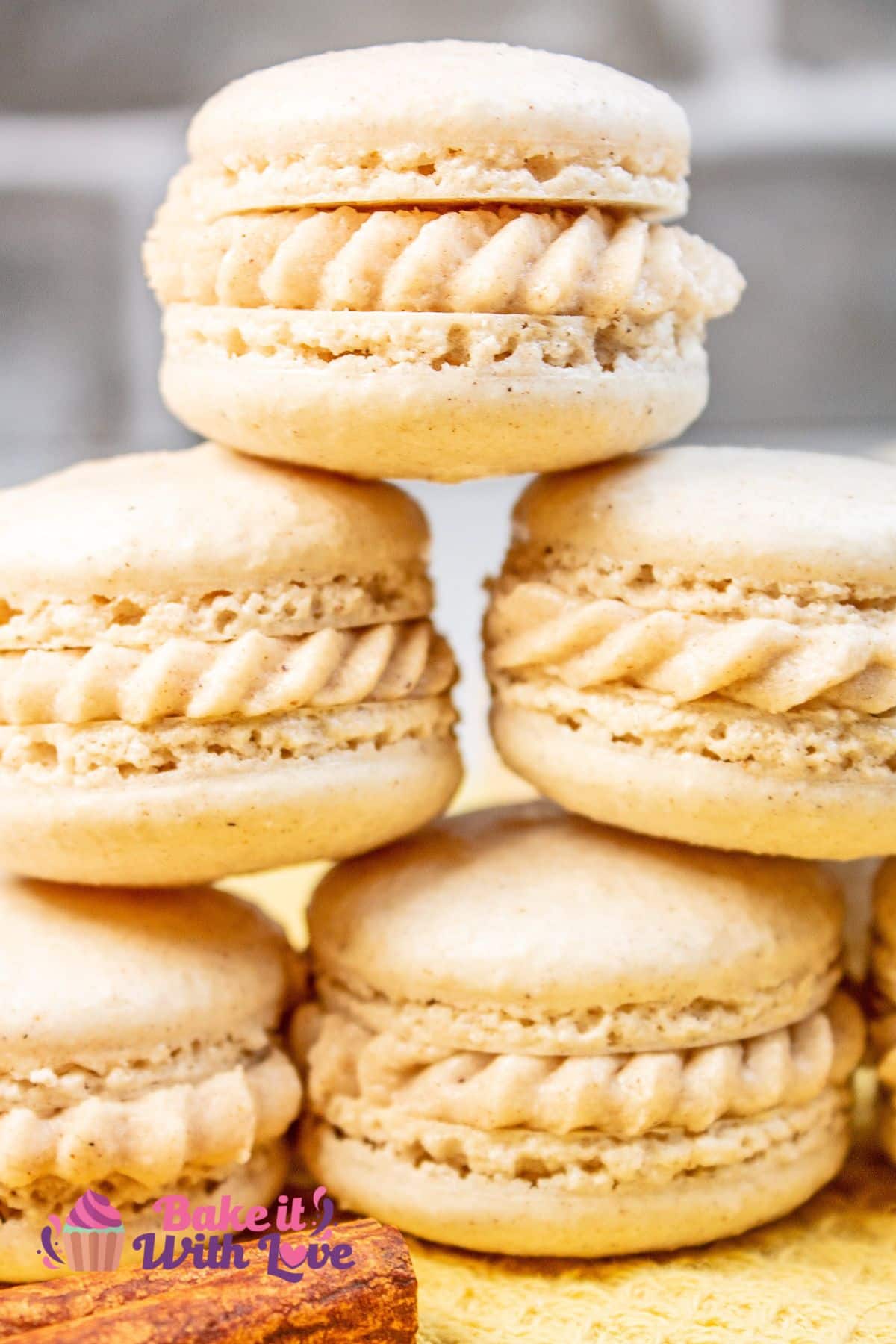 Tall image showing a pyramid of apple pie macarons on a yellow cloth with a cinnamon stick in front. 