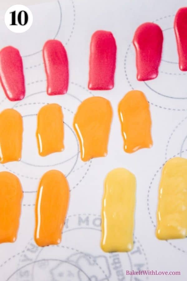 Turkey cake pops process photo 10 showing red, yellow, and orange chocolate feathers on a piece of parchment paper. 