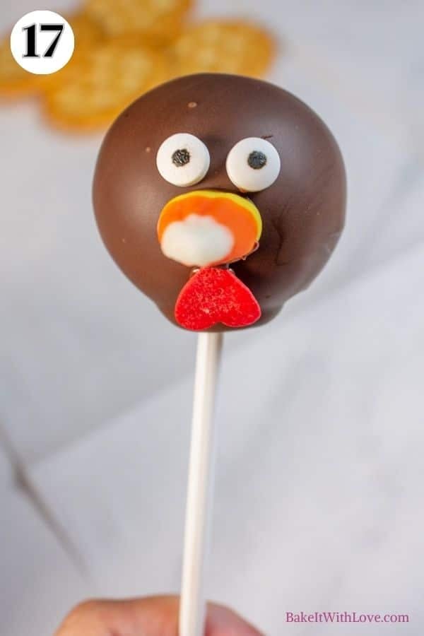 Turkey cake pops process photo 17 showing a brown cake pop with candy eyes, a piece of candy corn for a beak, and an upside-down heart sprinkle for a wattle.