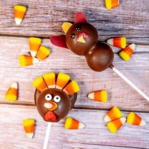 Square image showing two Thanksgiving turkey cake pops laying down surrounded by candy corn.