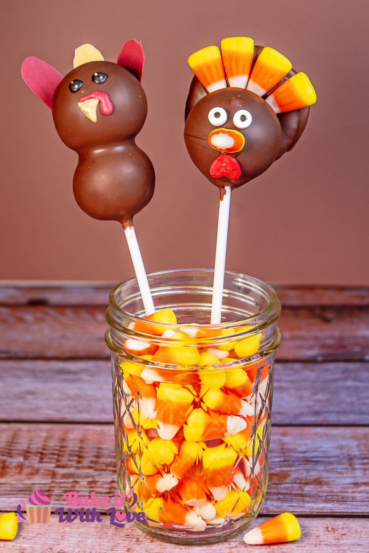 Tall image showing a stacked turkey cake pop and a candy corn turkey cake pop standing up in a glass filled with candy corn. 