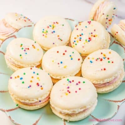 Square image of birthday cake macarons with sprinkles on a plate.