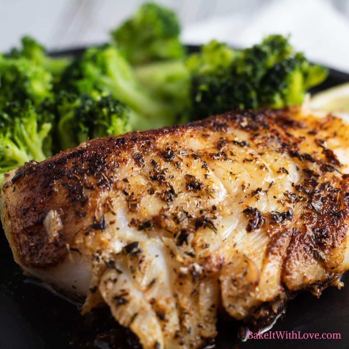 Square image of blackened cod fish on a black plate with broccoli.