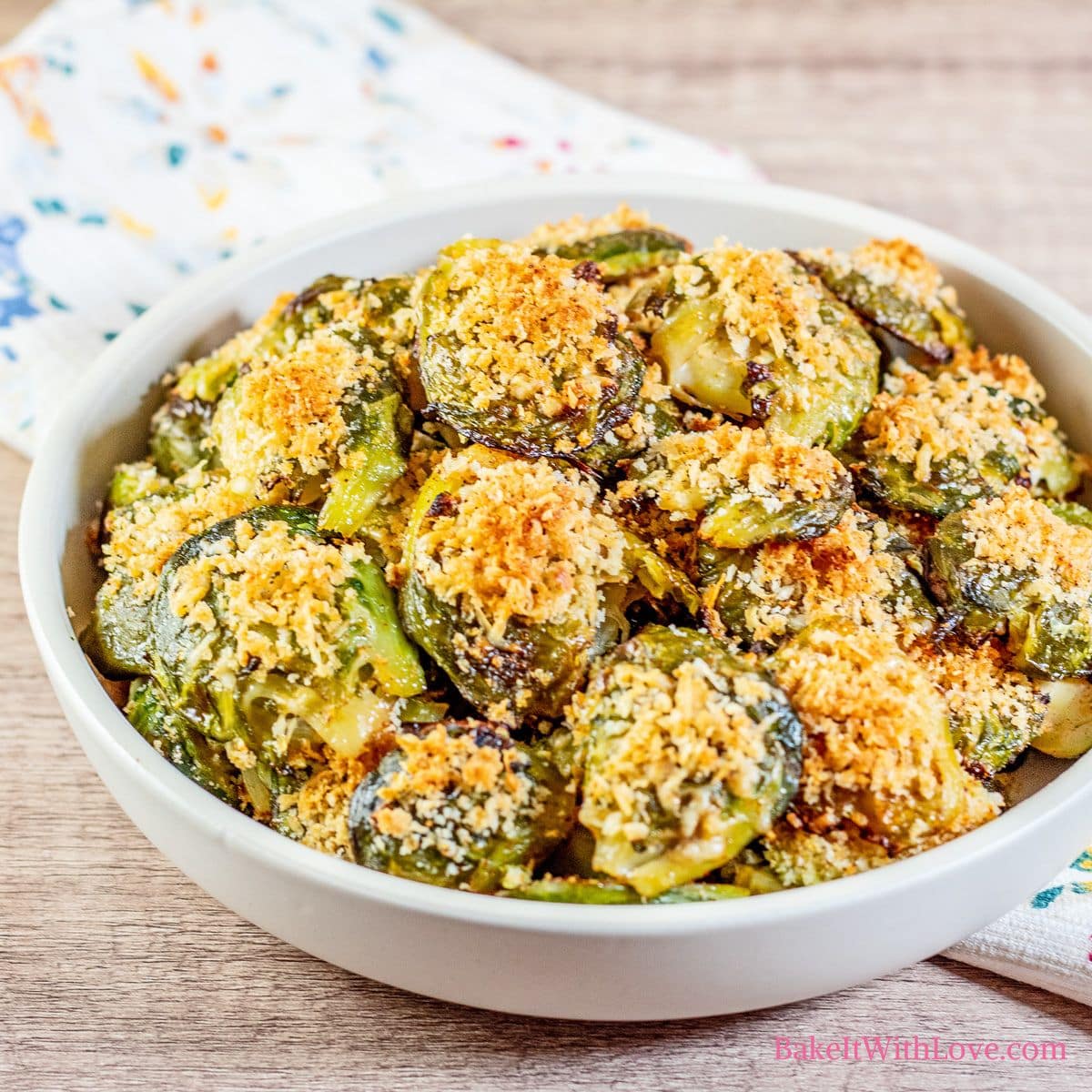 Square image of crispy parmesan smashed brussel sprouts in a bowl on a wooden surface with a napkin.