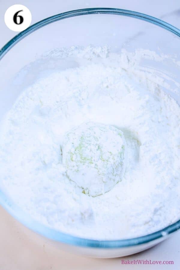 Grinch cookies process photo 6 showing a dough ball being rolled in confectioners sugar in a glass mixing bowl. 