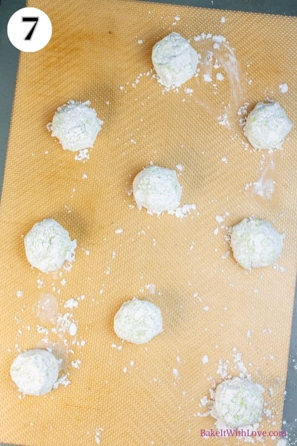 Grinch cookies process photo 7 showing unbaked dough balls covered with confectioners sugar spaced out on a silicone baking mat. 