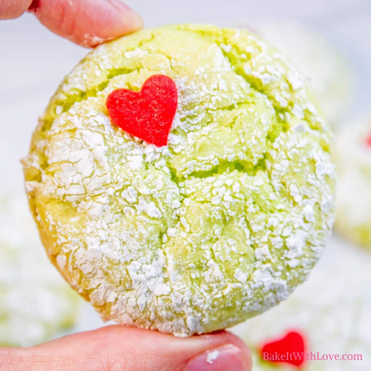 Square image showing a hand holding one of the grinch cookies with a heart sprinkle. 