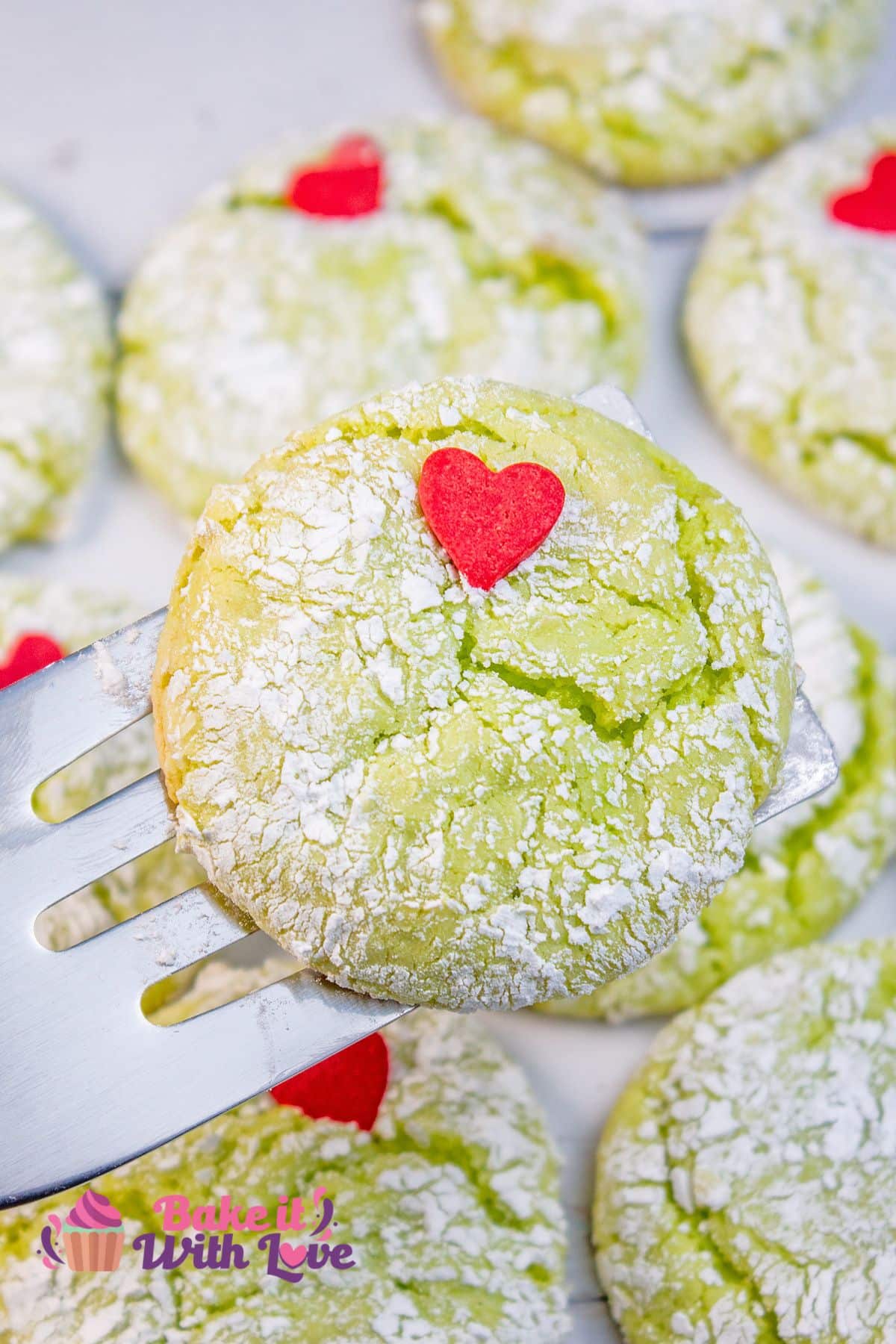 Tall image showing a Grinch cookie on a small metal spatula with more cookies in the background. 