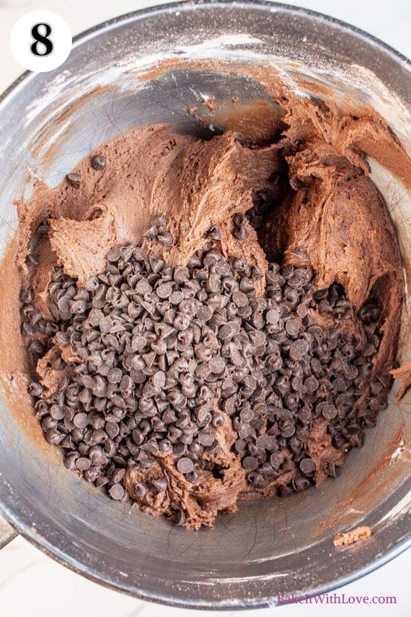 Hot chocolate cookies process photo 8 showing chocolate chips added to the dough in a metal mixing bowl. 