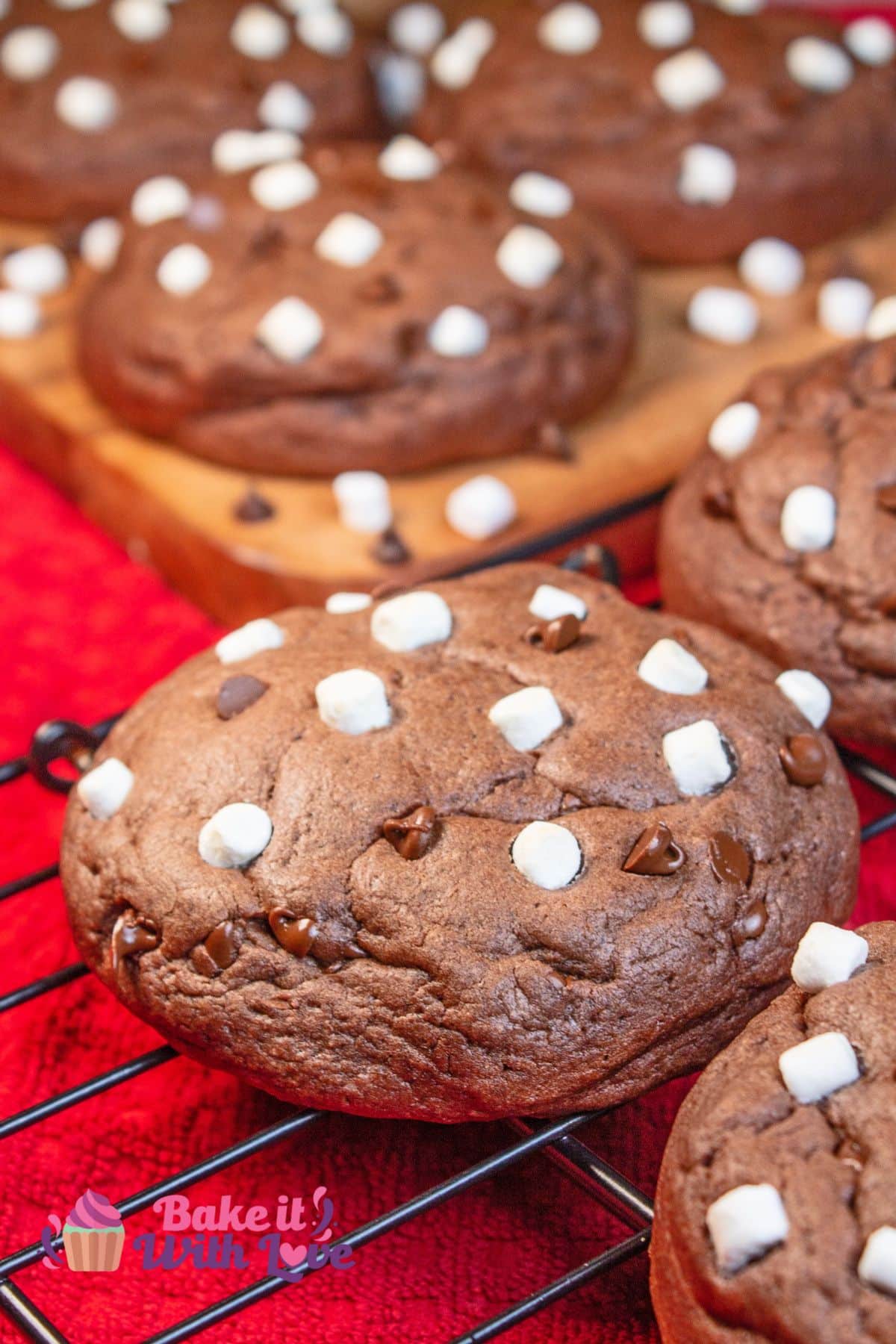 Tall image showing a hot chocolate cookie on a wire cooling rack with more cookies in the background on a wooden surface. 