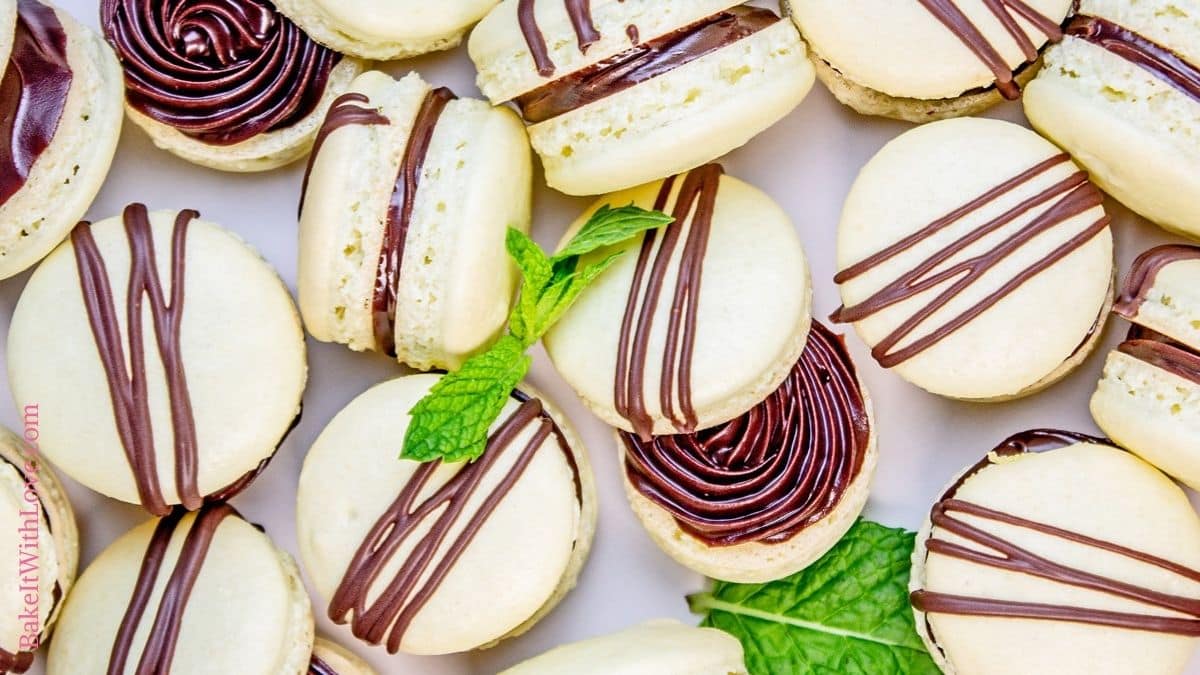 Wide image showing a bunch of mint chocolate macarons with some having the top skewed so you can see the filling and mint leaves.