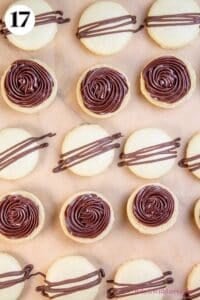 Mint chocolate macarons process photo 17 showing macaron shells on parchment paper where half are topped with chocolate ganache and the other half have a chocolate drizzle.