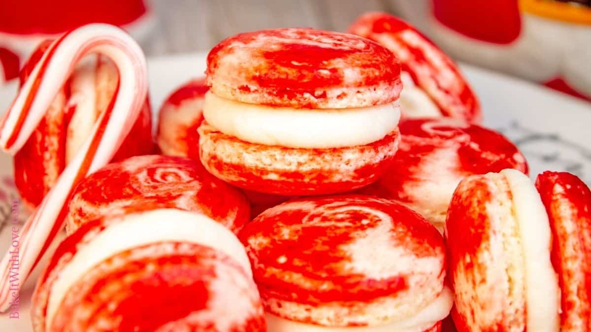 Wide image showing an up close shot of a stack of peppermint macarons and a candy cane. 