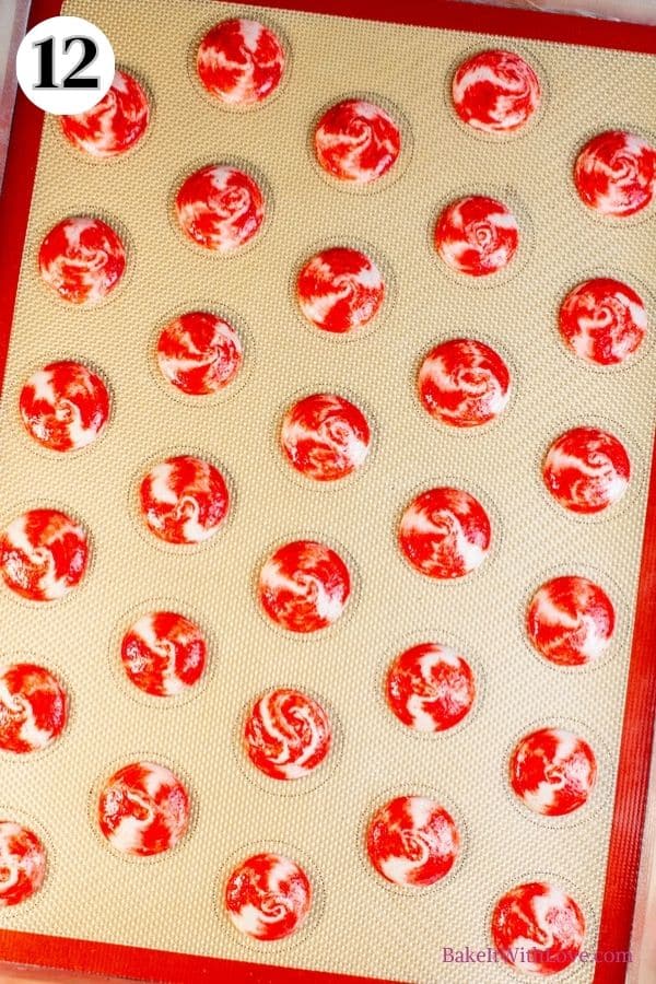 Peppermint macarons process photo 12 showing the unbaked, red and white swirled macaron shells on a silicone baking mat. 