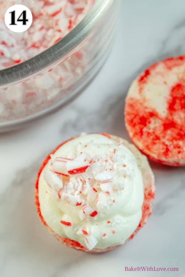 Peppermint macarons process photo 14 showing a macaron shell topped with ganache and crushed candy canes with a bowl of candy canes in the background. 