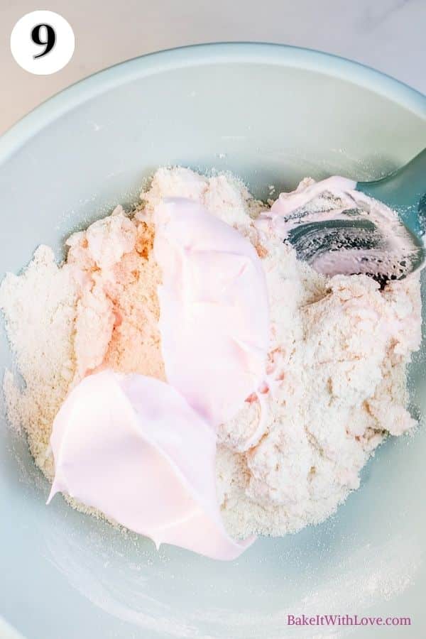 Strawberry macarons process photo 9 showing slightly mixed macaron batter with more meringue in a mixing bowl with a silicone spatula sticking out. 